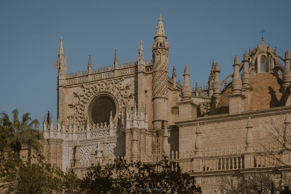 The Gothic structure of the Cathedral de Sevilla with a large circular mirror and pointed walls under clear blue skies. Wondering how many days in Seville? Explore the awe-inspiring architecture and rich cultural heritage of this vibrant city.