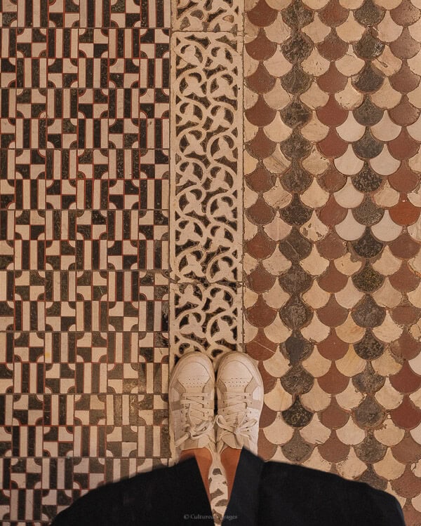 Close-up of a person's feet standing on the intricate and colorful mosaic flooring of the Florence Cathedral.