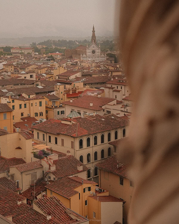 Aerial view of Florence, showcasing the city's red-tiled rooftops and the Basilica of Santa Croce in the distance on a misty day.