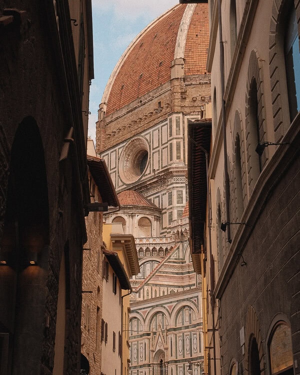View of the Florence Cathedral's dome framed by narrow, historic streets of the city.
