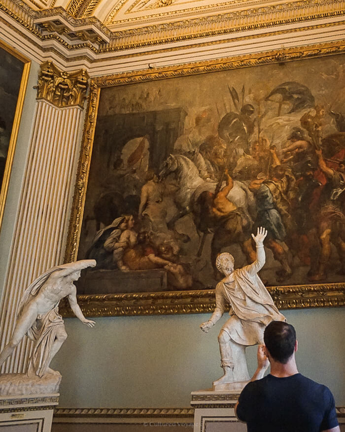 A large painting of The Triumphal Entry of Henry IV into Paris, with two statues positioned beneath it, capturing the grandeur of the historical event and the surrounding artistic elements.