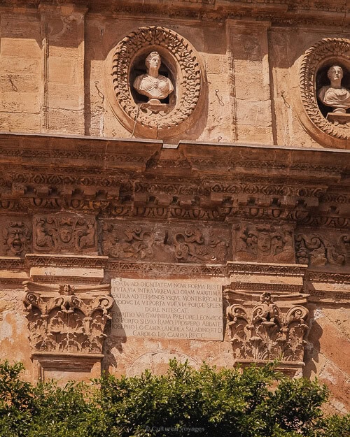A close-up of intricate stone carvings on a historic building in Palermo, Italy, showcasing classical busts and a Latin inscription, reflecting the city’s rich architectural history.