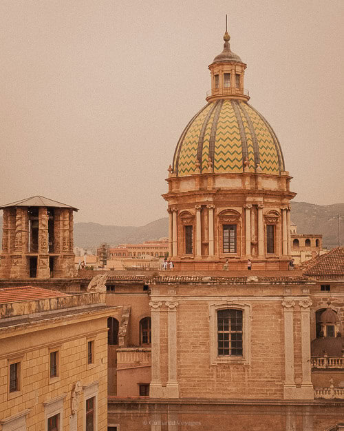 A view of a grand domed cathedral in Palermo, with mountains rising in the background, displaying the harmony between architecture and nature in the city.