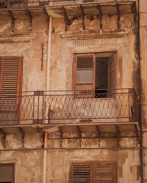 A weathered, rustic balcony on an old building in Palermo, showing wooden shutters and crumbling plaster, which add to the city’s historic charm.