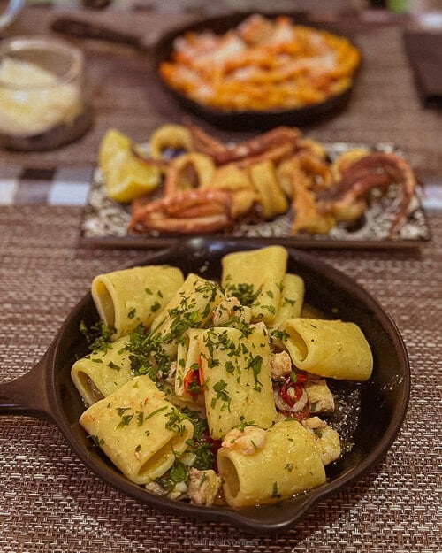A plate of Sicilian pasta garnished with fresh parsley, served with seafood and lemon, on a rustic wooden table.