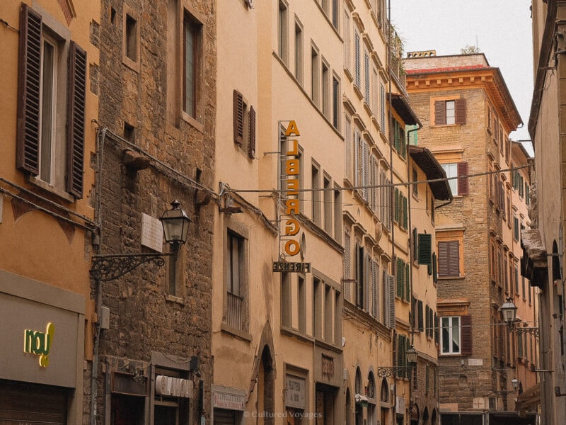 A narrow Florence street lined with stone and stucco buildings and wooden shutters.