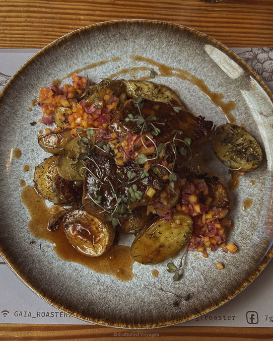 A plated dish of roasted potatoes and garnished meat, topped with fresh herbs and colorful vegetables, served at a Porto restaurant.