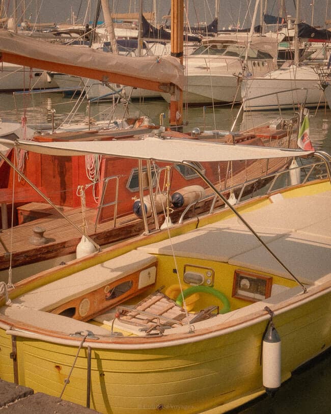 A small yellow boat with a white canopy docked among other sailboats in a peaceful marina on Procida Island, bathed in soft sunlight.