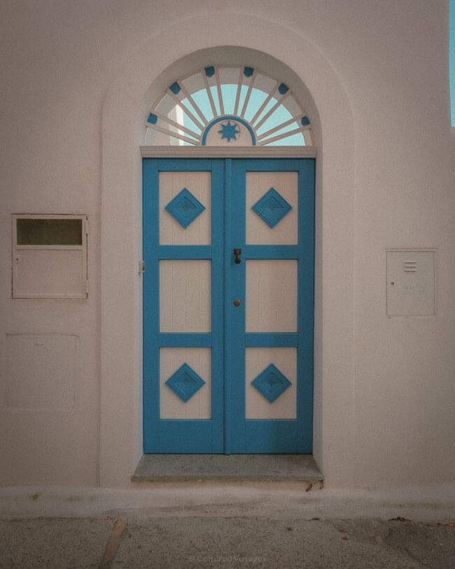 Decorative blue and white double door with geometric panels and a fan-shaped window above in Ischia, Italy.