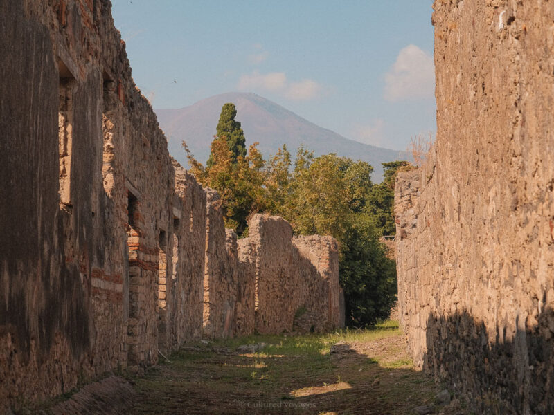 An ancient street between stone buildings, with Mount Vesuvius beyond.