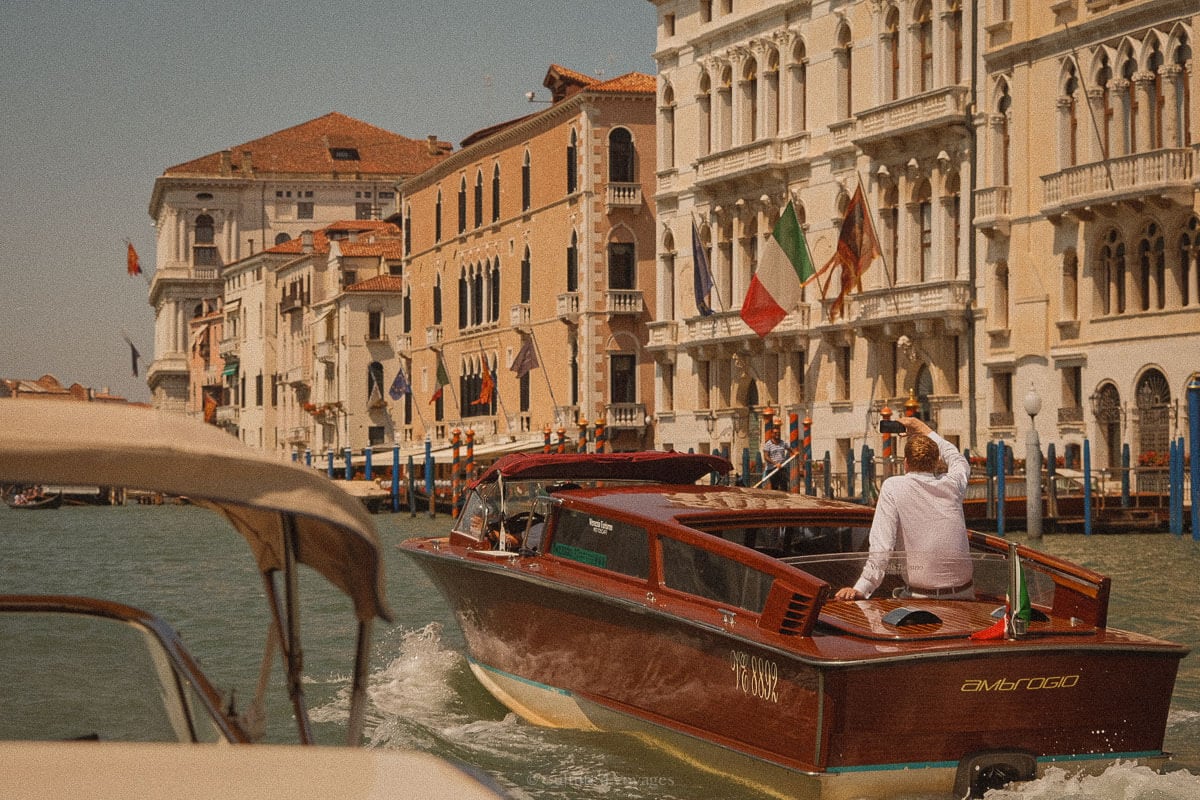 A close-up of a historic Venetian buildingโs arched doorway, partially submerged in canal water. The aged red brick and peeling plaster contrast with the ornate white stone arch, a reminder of the city's centuries-old architecture and its ongoing battle with rising water levels.