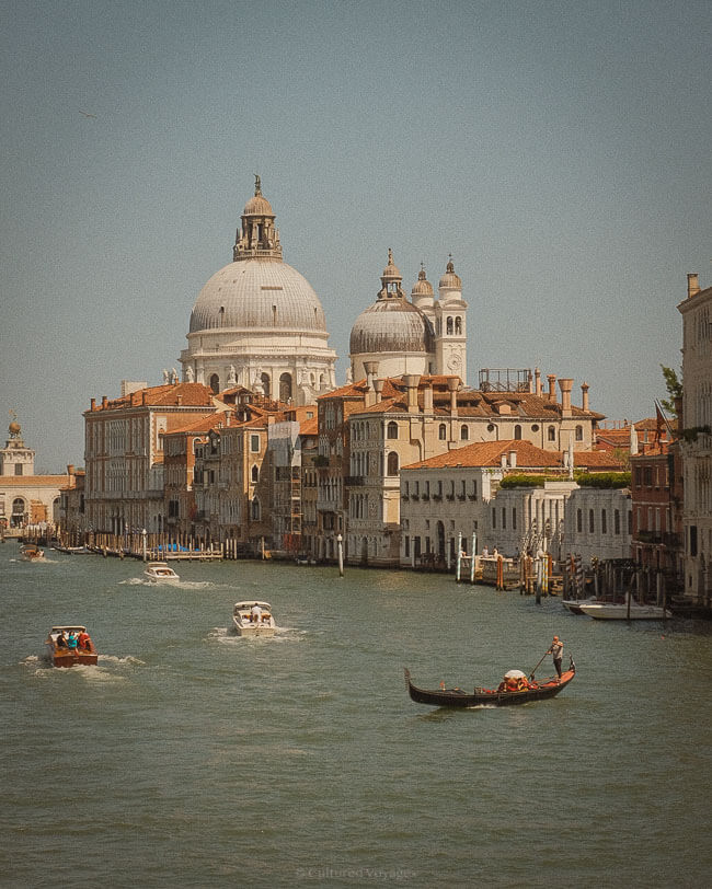 Boats and gondolas navigate the Grand Canal in Venice, with the domed Basilica di Santa Maria della Salute towering over the waterfront—an iconic view when deciding Florence or Venice First.