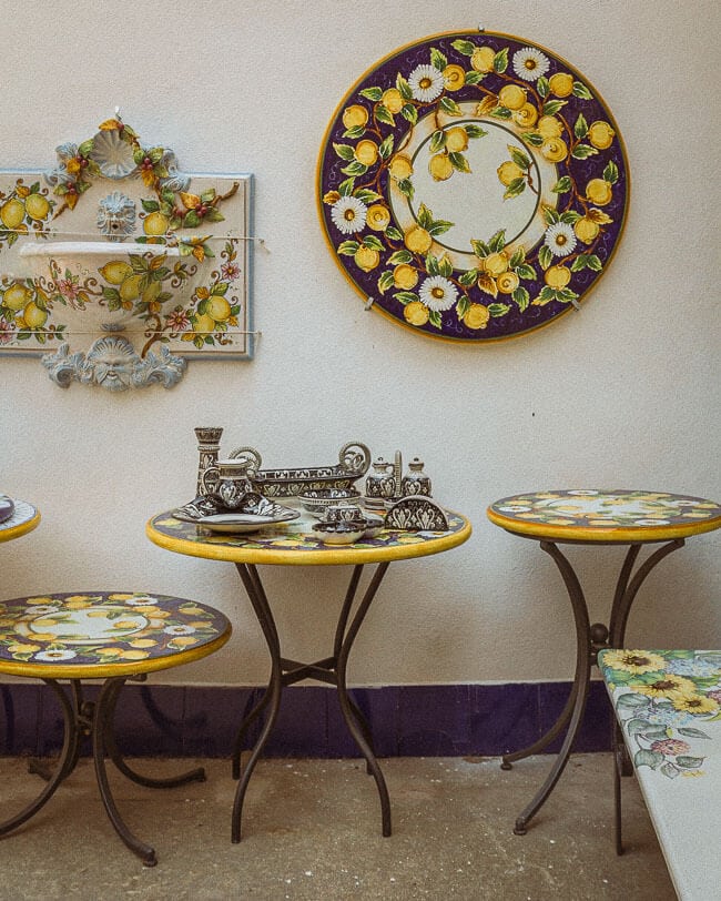 A display of hand-painted ceramic tables and wall hangings adorned with lemon motifs and floral designs, arranged in a charming artisan courtyard in Ravello.