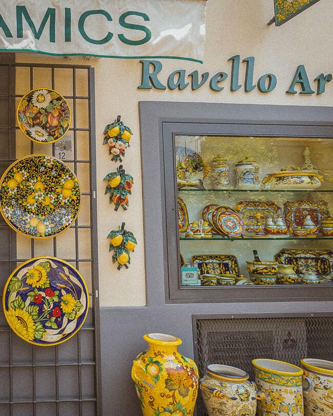 A colourful ceramic shopfront in Ravello showcasing intricately painted lemon-themed plates, vases, and pottery through a display window and on the exterior wall.
