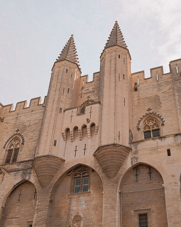 Close-up of the gothic towers and arched windows of the Palais des Papes, emphasising the vertical lines and fine medieval stonework against a soft sky.