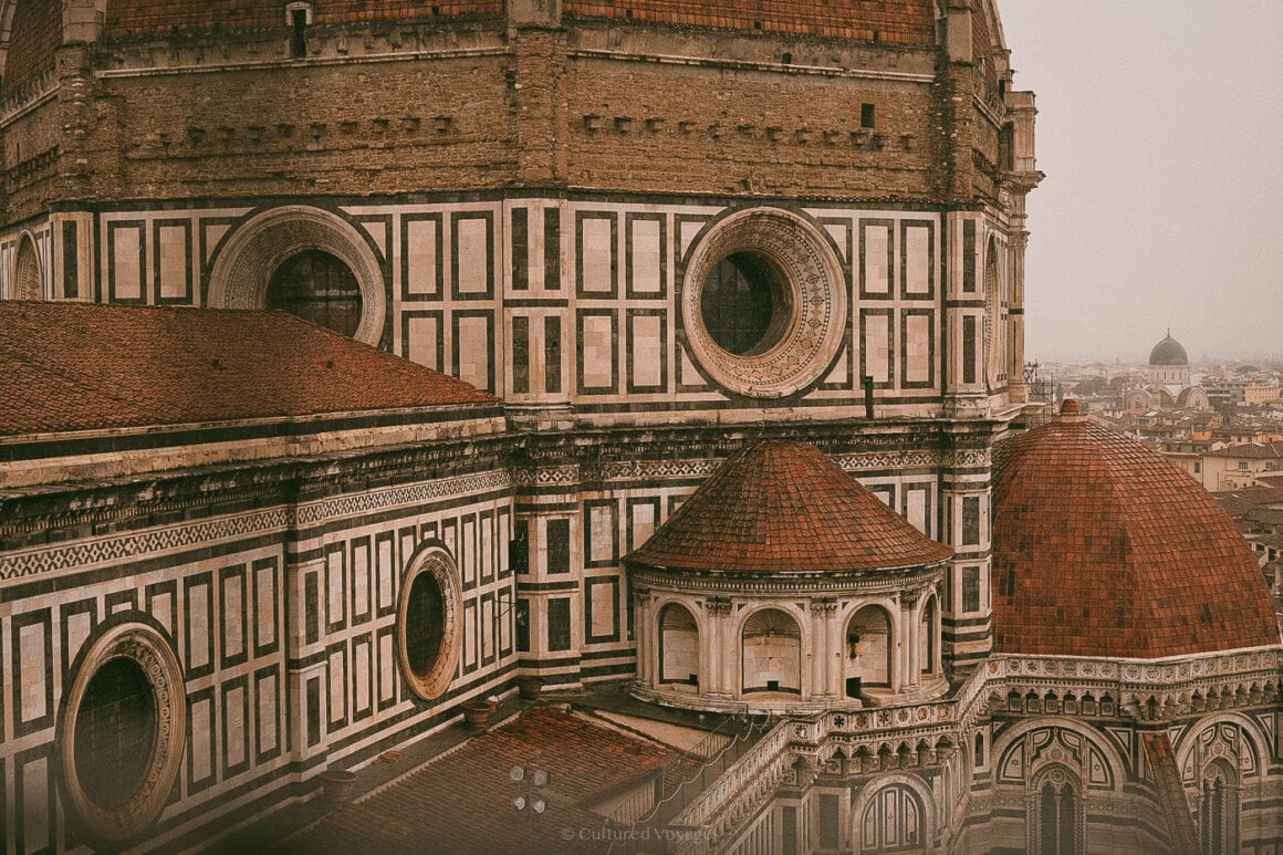 Detailed view of the Florence Cathedral's marble facade and iconic red domes under overcast skies, showcasing Renaissance architectural grandeur.