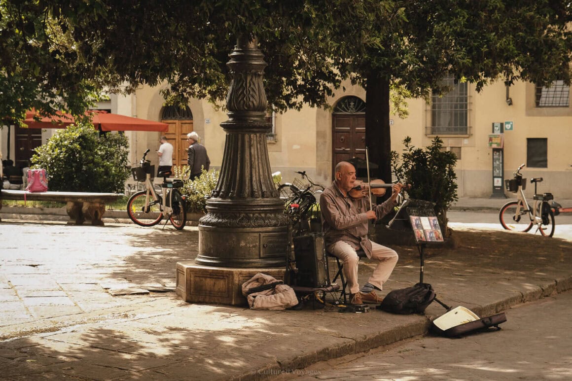 Elderly violinist performing under the shade of a tree in a peaceful Florentine piazza in the Oltrarno district.