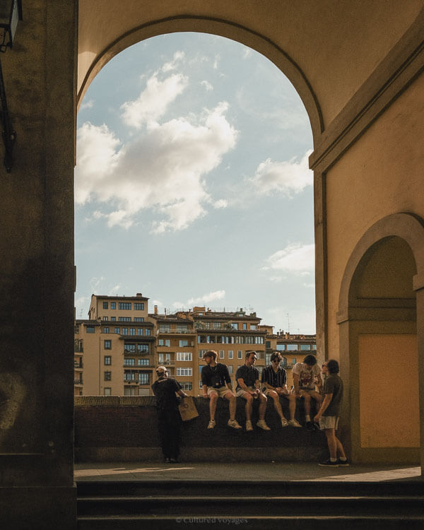A group of friends relax under a large stone arch with city buildings in the background, enjoying the calm ambience during the best time to visit Florence.