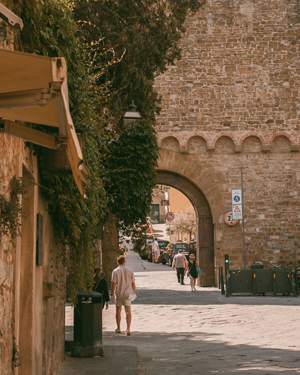 People walking through a sunlit medieval stone arch in Florence, capturing the best time to visit Florence with its warm golden hour tones.