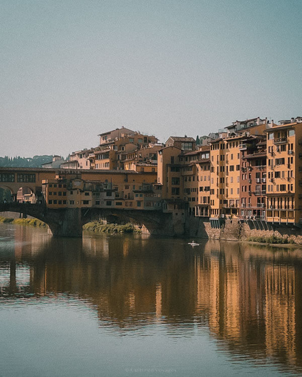 Warm afternoon light reflects off Ponte Vecchio and surrounding buildings over the Arno River, a peaceful scene showcasing the best time to visit Florence.