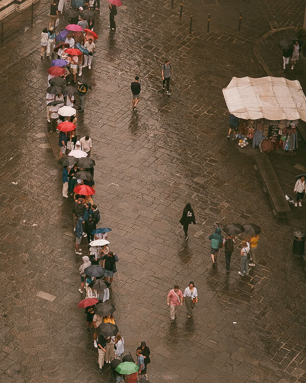 People holding colorful umbrellas line up outside the Florence Cathedral on a rainy day, proving that even during showers, itโs still the best time to visit Florence.