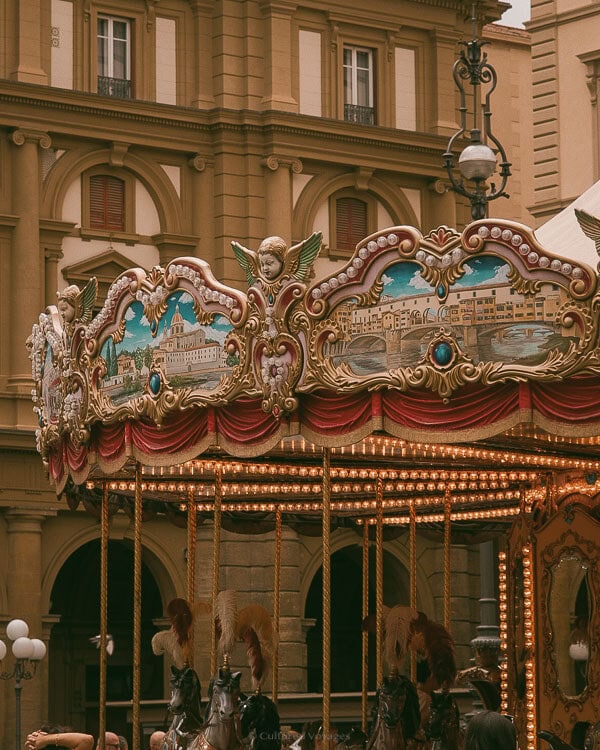 Ornate vintage carousel with angelic figures and painted panels in Piazza della Repubblica, Florence, glowing with warm lights.