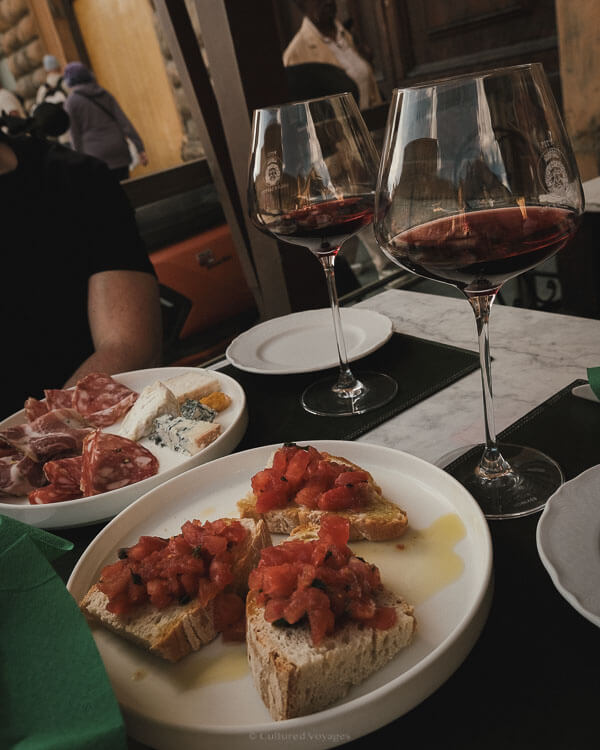 Close-up of bruschetta, assorted meats, cheeses, and two glasses of red wine, the perfect pairing for a relaxing afternoon during the best time to visit Florence.