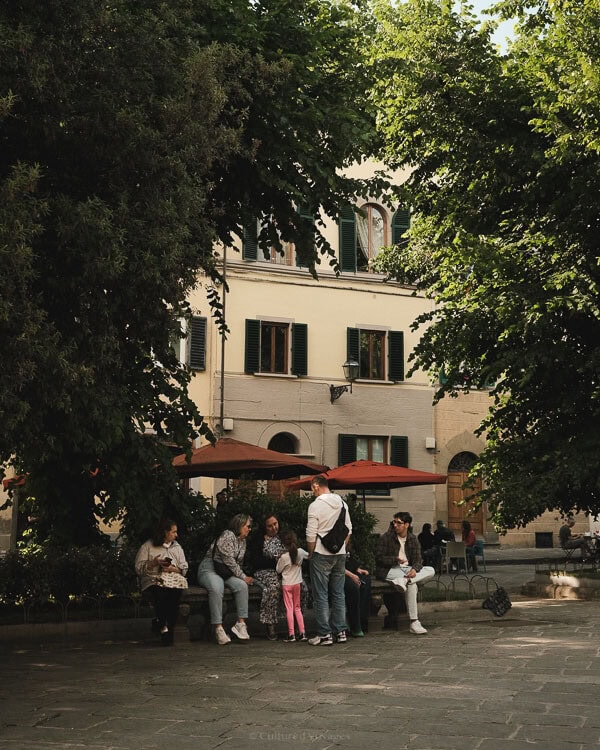 Locals enjoy a calm afternoon on benches under trees in a serene square in Florence, embodying the best time to visit Florence for a slower pace.