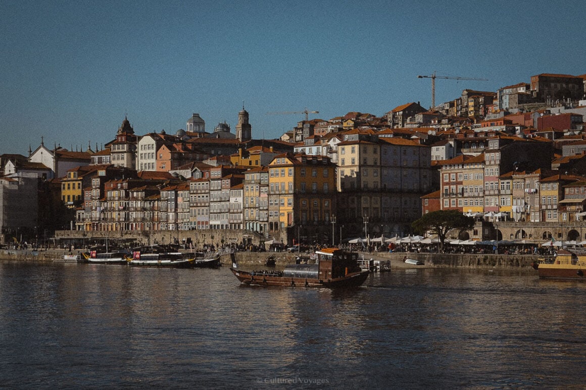 A scenic view of Porto’s colourful Ribeira district with traditional boats floating on the Douro River beneath a clear winter sky, capturing the essence of Portuguese charm.
