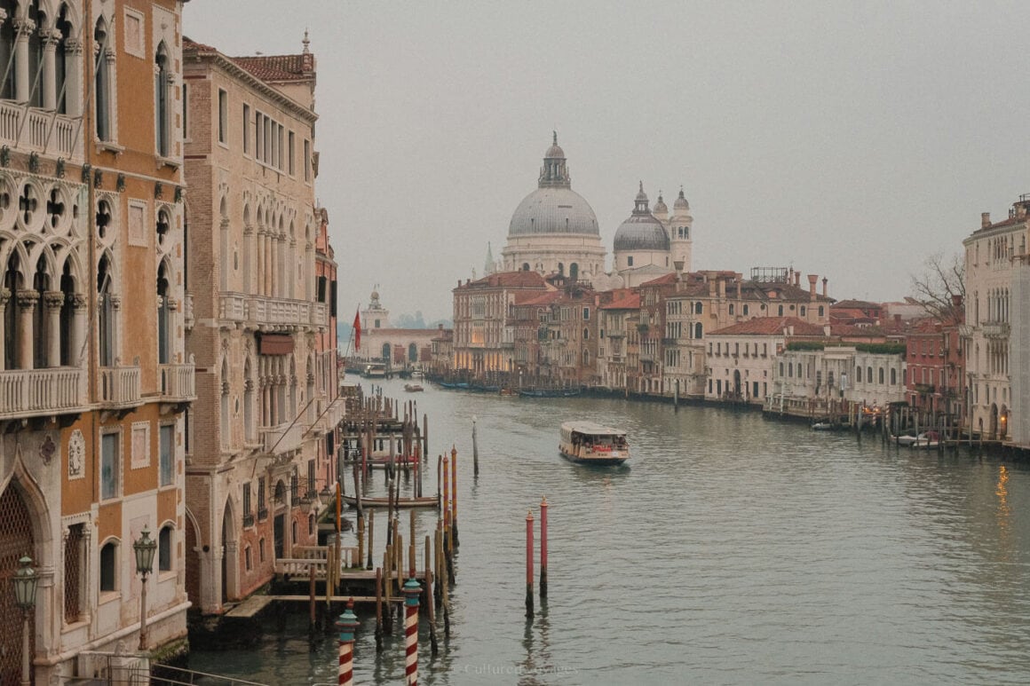 A vaporetto glides along the Grand Canal in Venice, flanked by elegant palazzos and crowned by the domes of Santa Maria della Salute beneath a soft, misty winter sky.