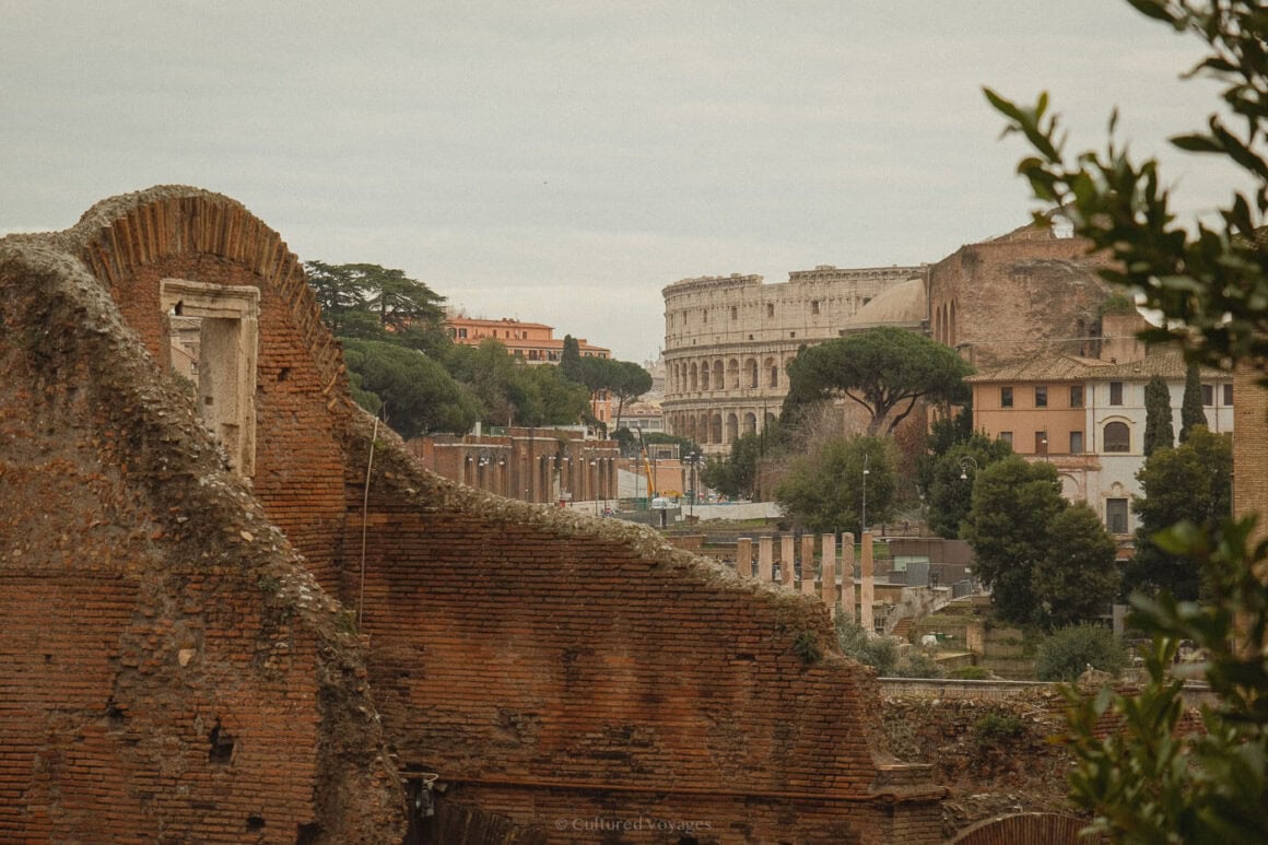 A wintry perspective of the Colosseum rising behind layers of ancient ruins and stone walls, showcasing why Rome remains one of the best European cities to visit in winter.