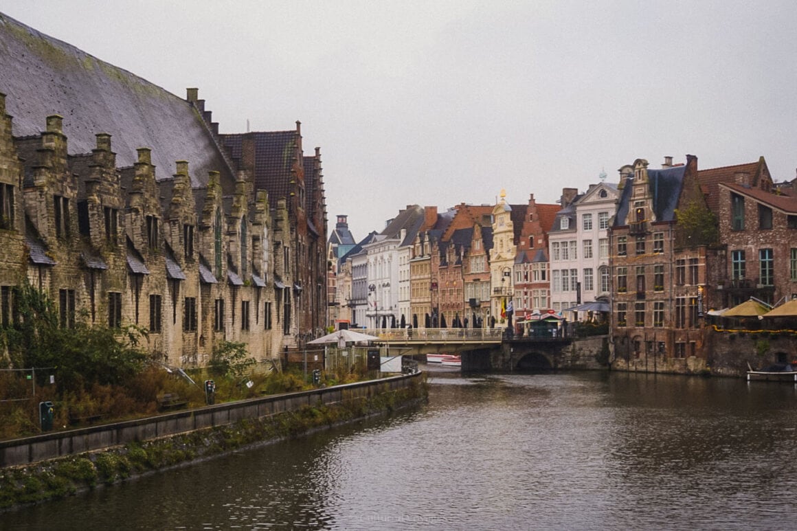A calm waterway winds through Ghent’s mediaeval city centre, bordered by centuries-old guild houses and stone façades on a grey winter’s day in Belgium.