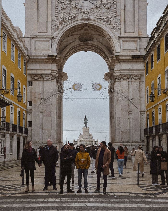 People gather beneath the grand Rua Augusta Arch in Lisbon’s city centre, an architectural highlight of one of the best European cities to visit in winter.