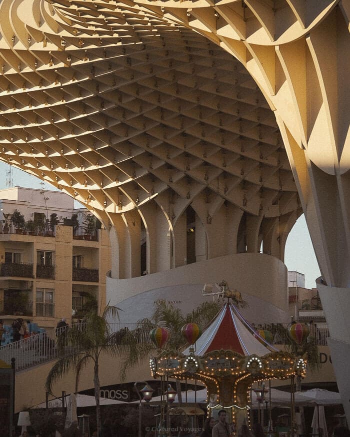 The striking wooden lattice of the Metropol Parasol contrasts with a colourful carousel below in the lively city of Seville, Spain.