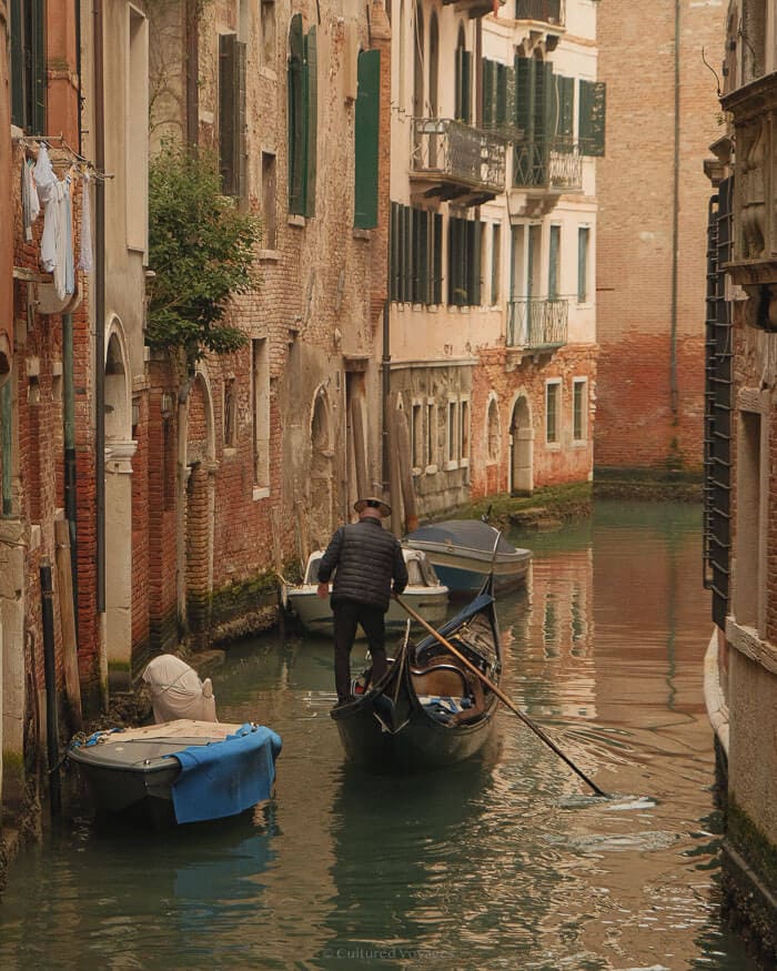 A gondolier steers a gondola along a peaceful canal surrounded by rustic buildings in Venice, one of the best European cities to visit in winter for its romantic charm and serene atmosphere.
