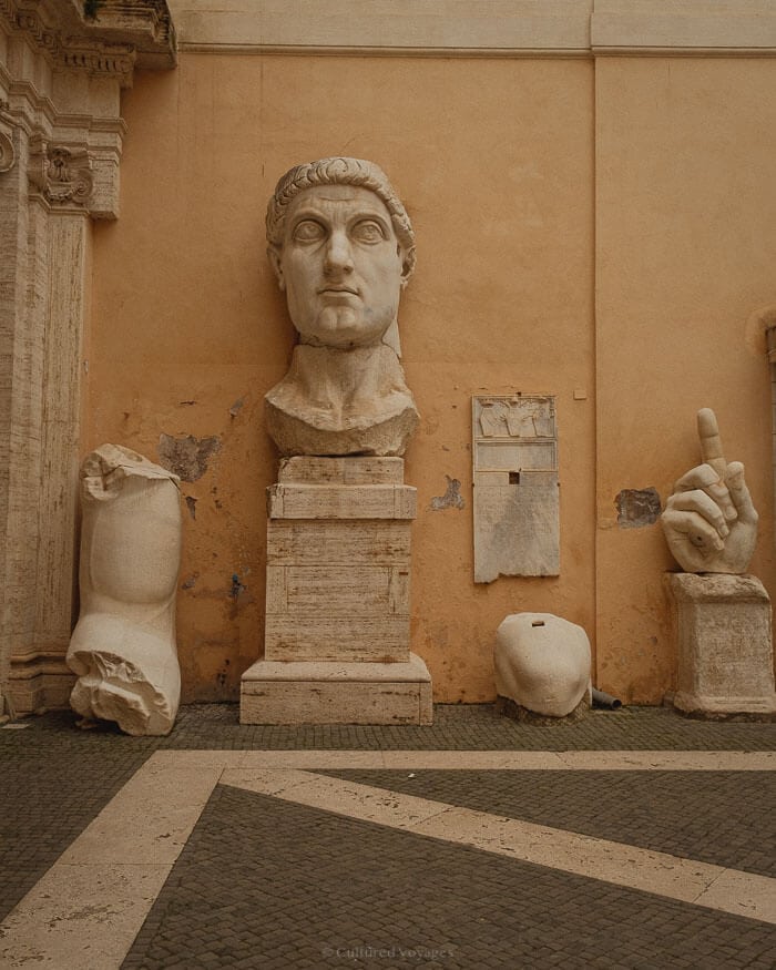 Massive fragments of a Roman statue displayed against an ochre wall in Rome, a reminder of the city’s ancient past and rich cultural heritage.