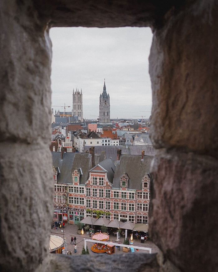 A view of Ghent’s old town and cathedral towers framed by a stone window, offering a unique perspective on this Belgian city’s winter charm.