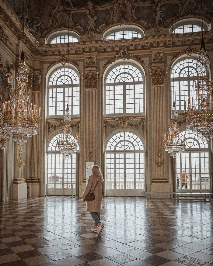A woman walks through a magnificent hall with glittering chandeliers and towering arched windows, reflecting the grandeur of one of the best European cities to visit in winter.