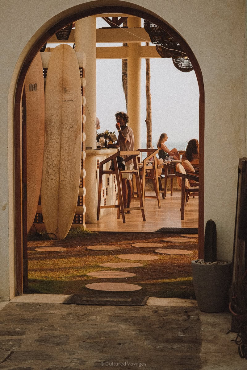 Arched entrance framing a beach bar with a surfboard and guests at Ahangama Beach in Sri Lanka.
