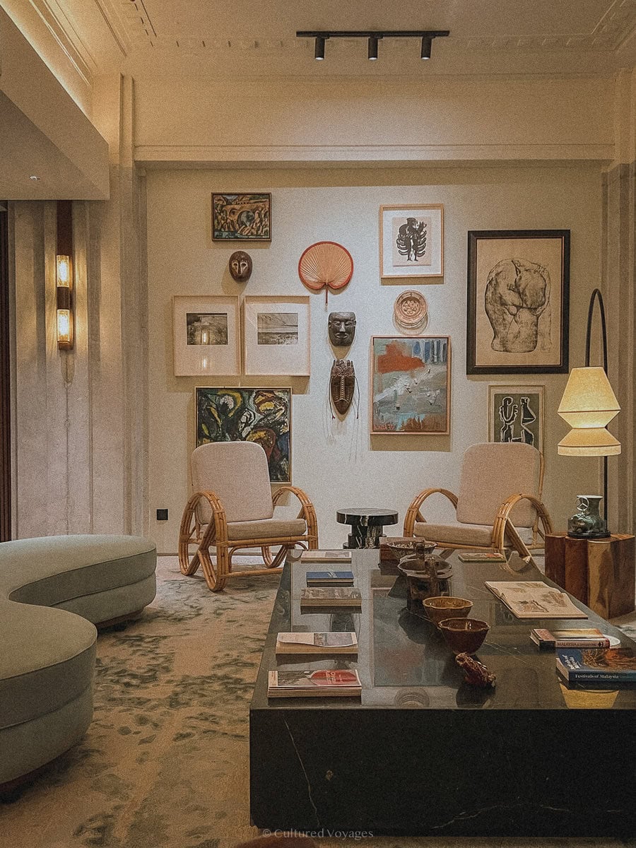 Art-filled reception lounge at Else Hotel in Kuala Lumpur, with rattan chairs and a long dark table.