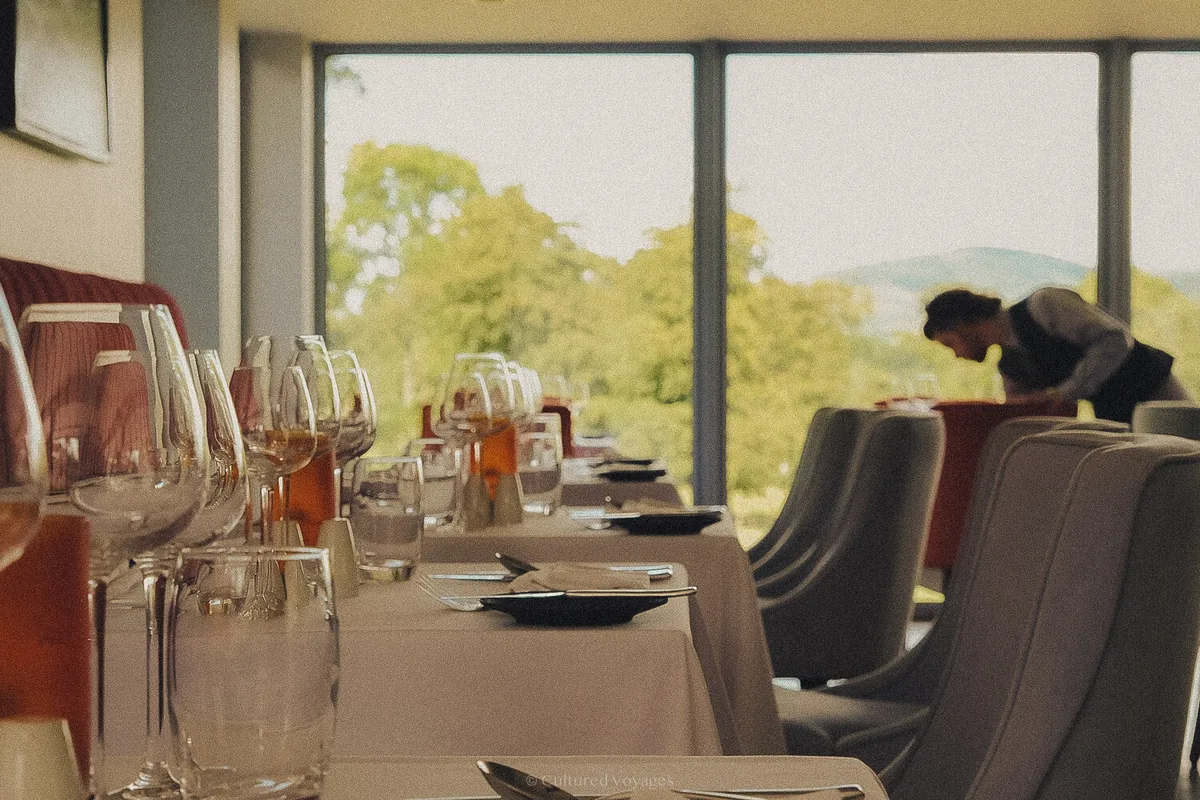 Dining tables set with wine glasses at Killeavy Castle, with a staff member preparing a table by the windows.
