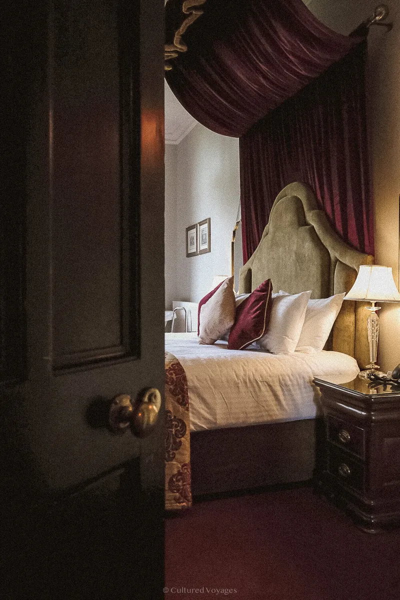Four-poster bed with plum drapery glimpsed through an open door at Markree Castle.