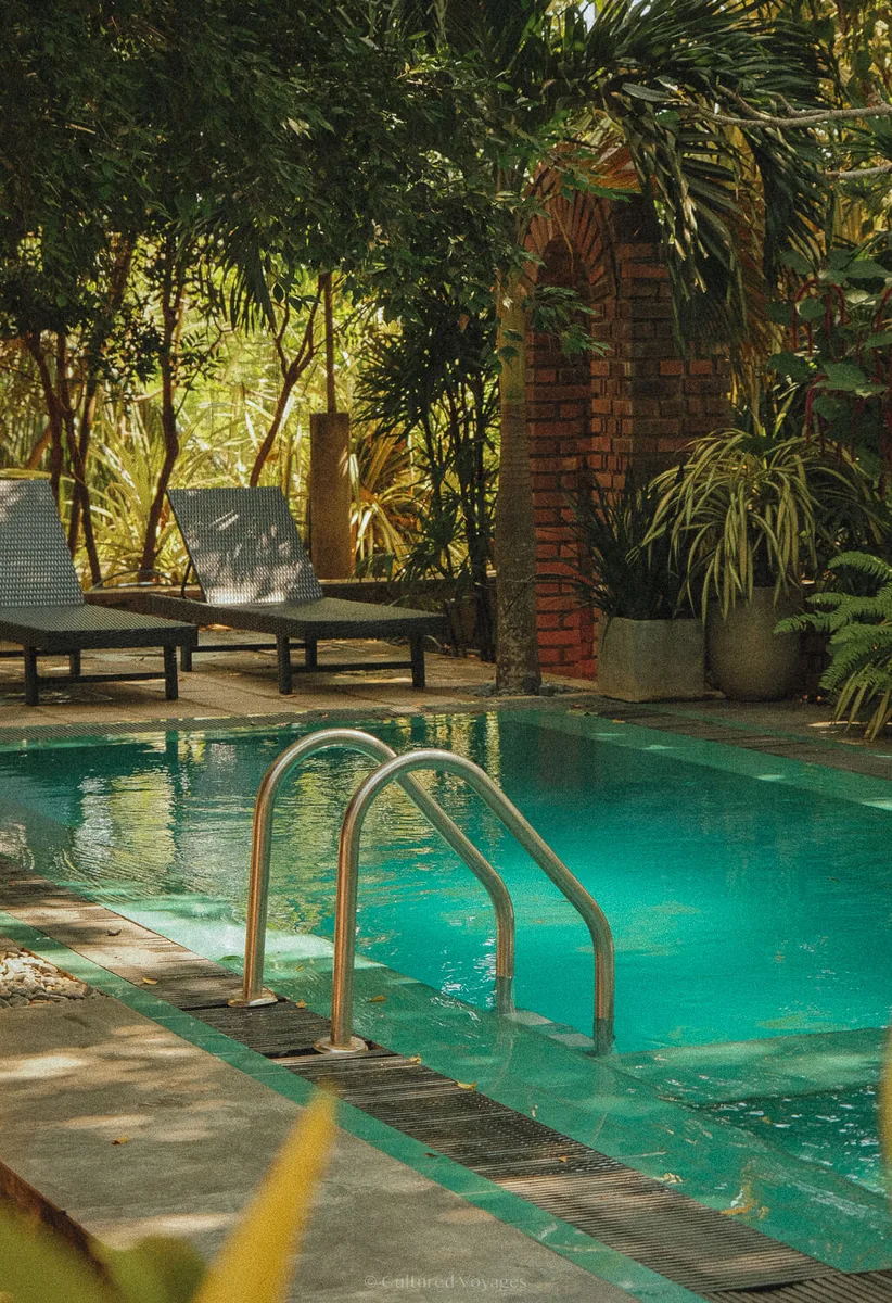 Turquoise hotel swimming pool and shaded loungers among tropical plants in Sri Lanka.