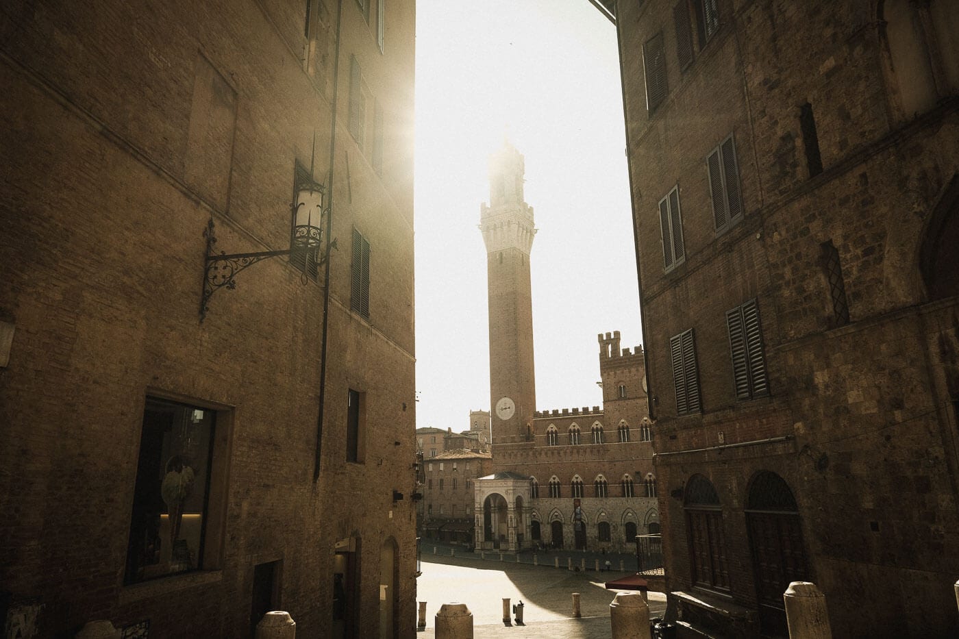 Sunlight above the Torre del Mangia and Piazza del Campo, framed by a narrow street in Siena.
