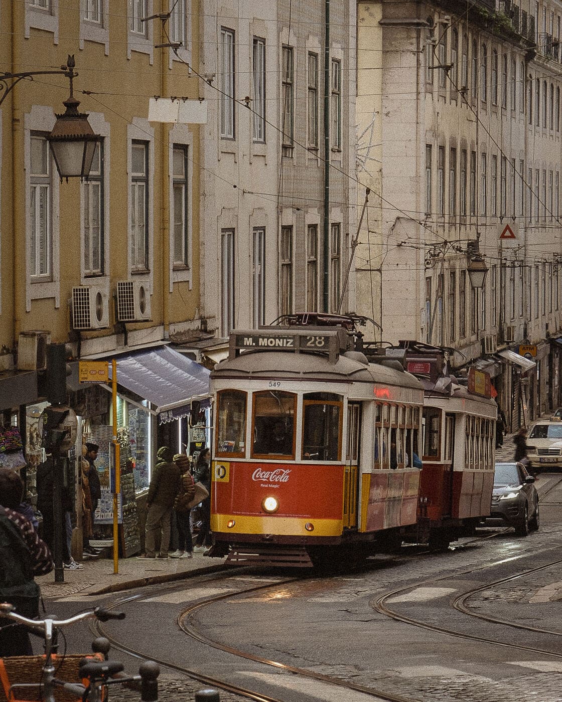 A number 28 tram travelling between the historic buildings of a Lisbon street.