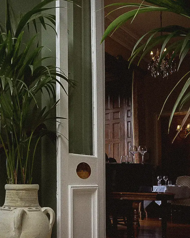 Doorway from the atrium with a potted palm and stone urn, the dining room beyond
