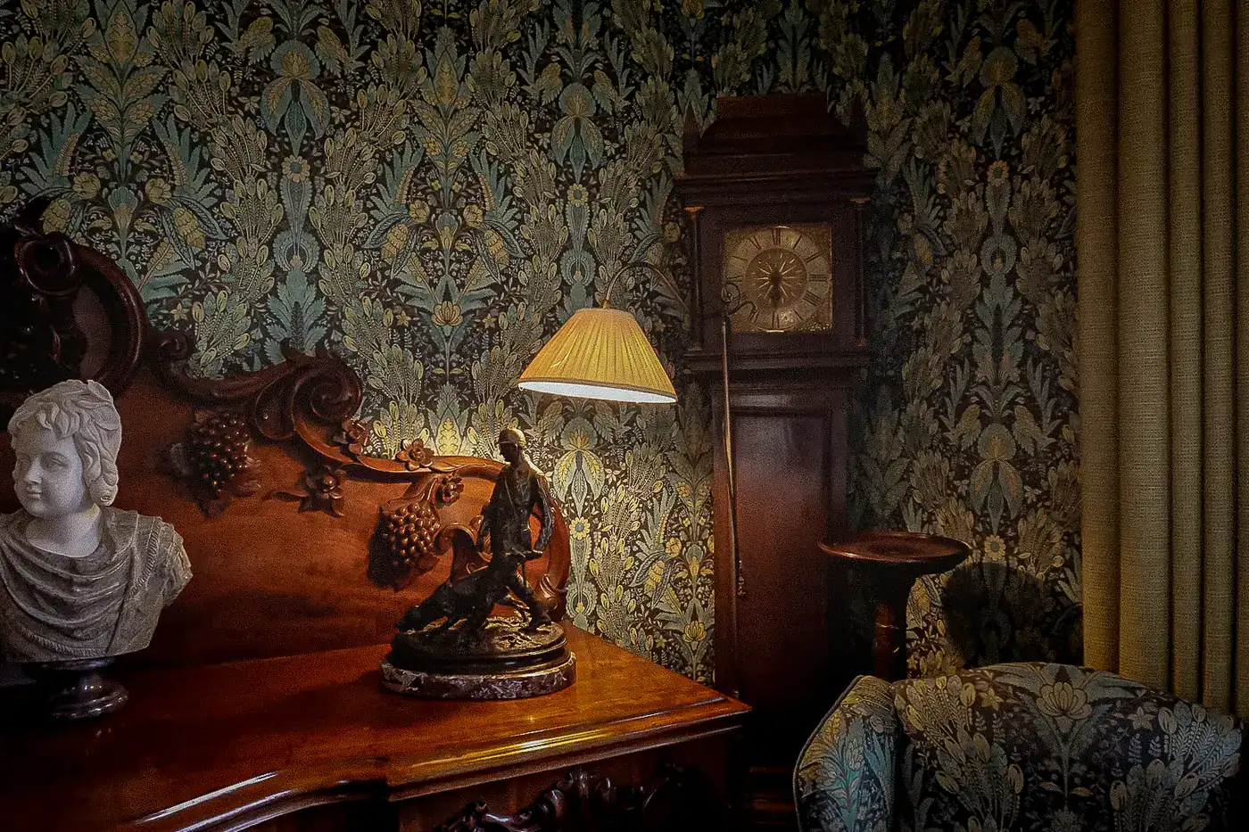 Carved sideboard with a marble bust, a lamp and a longcase clock against damask wallpaper