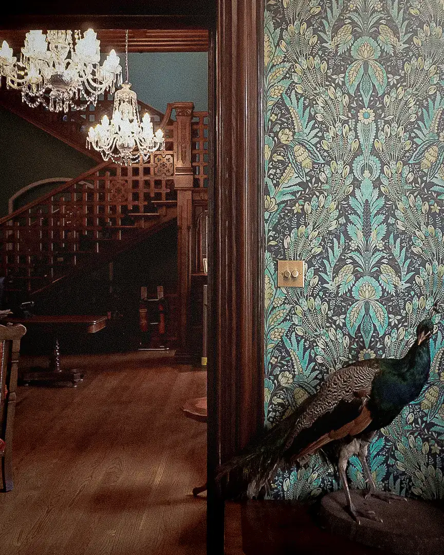 A mounted peacock beside a doorway opening onto the staircase and chandeliers