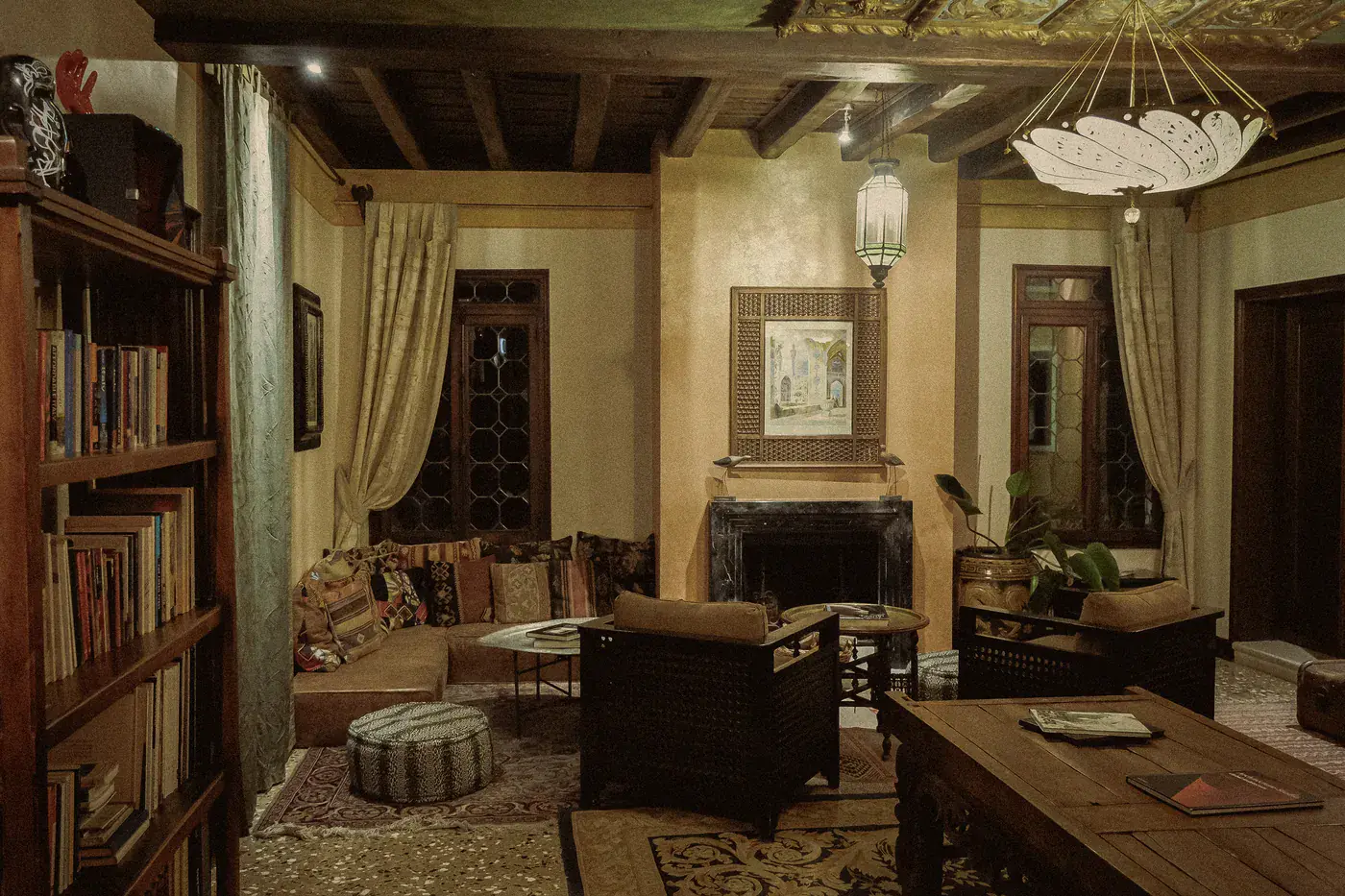 The first-floor lounge, with a bookcase, a sofa heaped with cushions, latticed armchairs and a fireplace beneath a framed painting