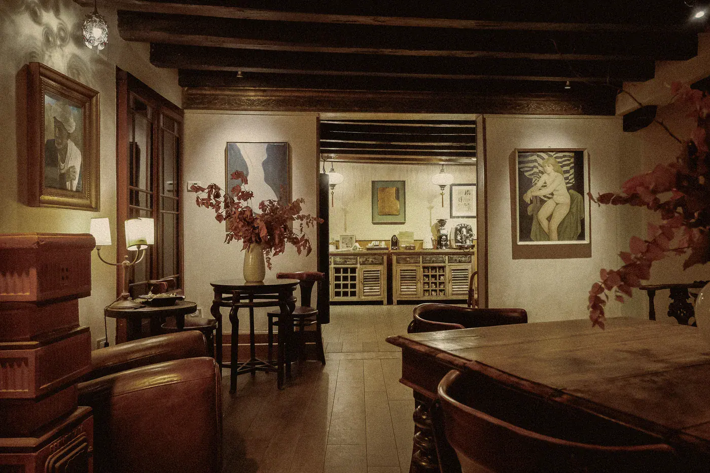 The ground-floor lounge at Novecento, with leather armchairs, a wooden table and autumn foliage, and the breakfast sideboards through the doorway